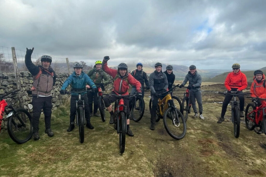 A group of riders standing with their bikes high up in the hills of the Lake District.